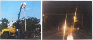 Grúa elevadora instala panel solar y equipo de control en poste semafórico; vista nocturna de la intersección intervenida.
