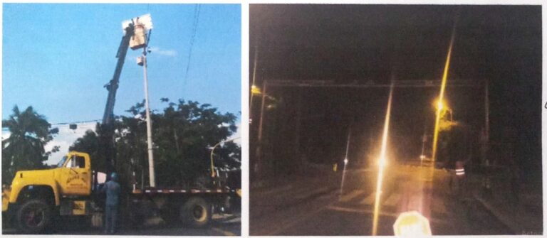 Grúa elevadora instala panel solar y equipo de control en poste semafórico; vista nocturna de la intersección intervenida.