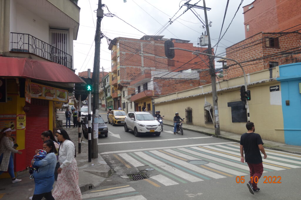 Intersección urbana de Caldas (Antioquia) con varios semáforos LED en rojo y postes rayados; cables aéreos visibles sobre la vía.