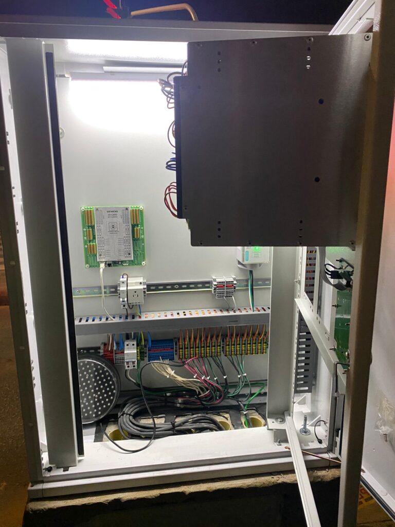 Gabinete eléctrico nuevo sobre pedestal, delimitado con conos y cinta de seguridad, en una intersección nocturna con semáforos LED en rojo y verde en Tunja.