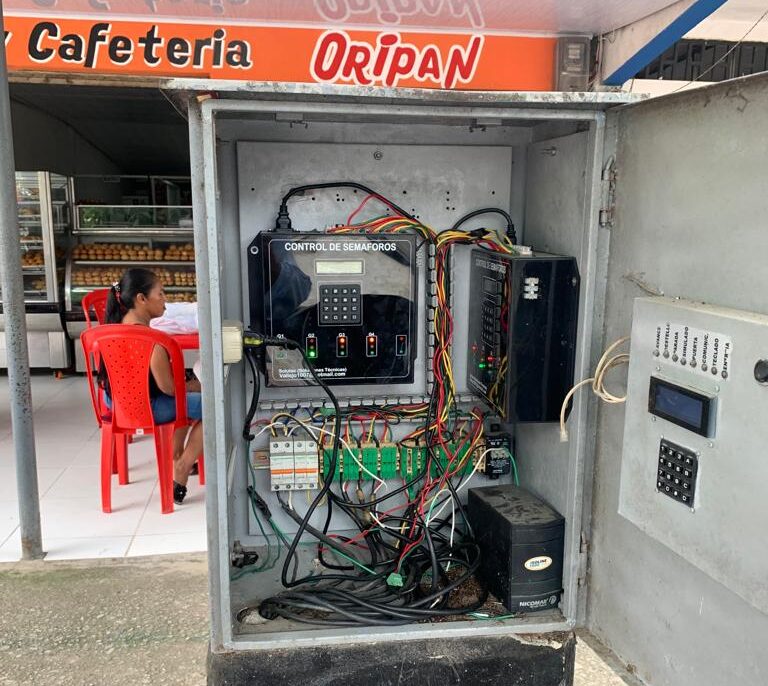 Caja de control abierta con cables desordenados, tarjeta de controlador alámbrico y UPS del sistema semafórico en Orito.
