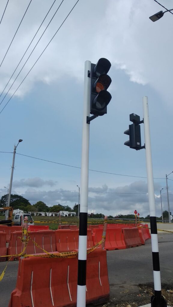 Vista de semáforo vehicular LED en verde sobre poste blanco y negro en la intersección Caracolí, Unidad Funcional 5.