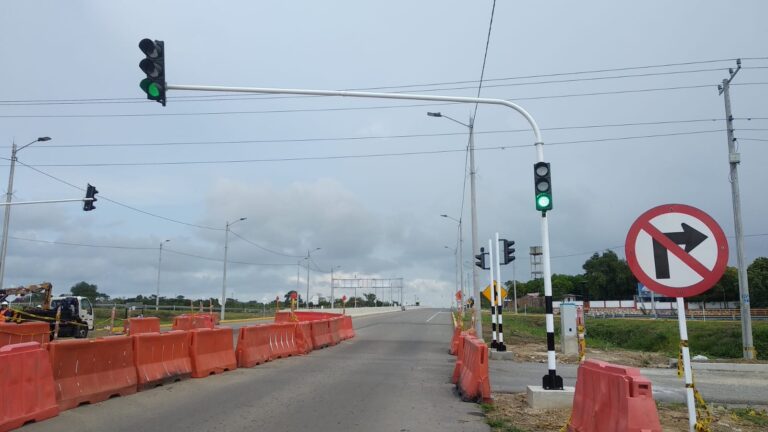 Vista panorámica de la intersección con semáforos instalados, barreras naranjas de obra y cableado aéreo de señalización peatonal.