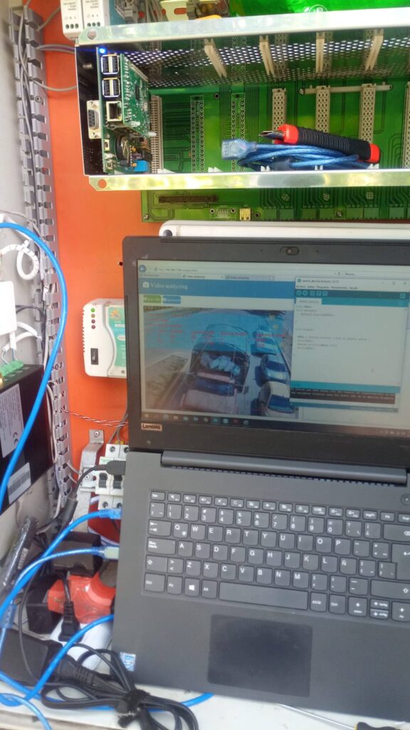 Interior de panel de control semafórico abierto, mostrando tarjeta electrónica y portátil con software de video‑análisis de tráfico.