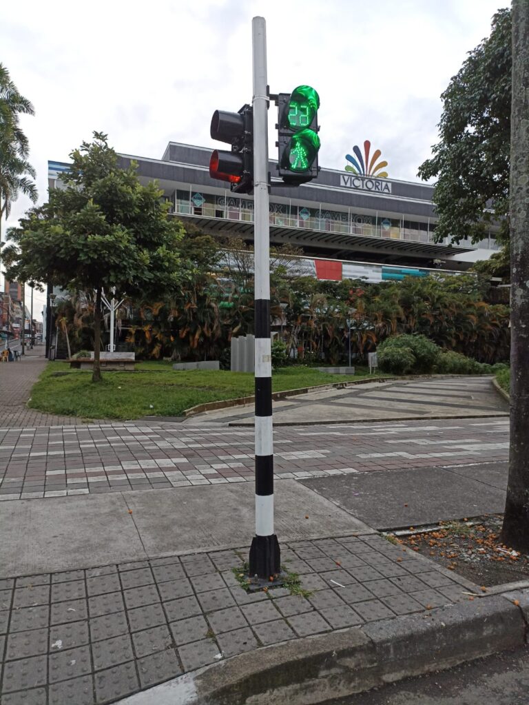 Semáforo peatonal con cronómetro verde frente al centro comercial Victoria en Pereira, con tachas viales y delineadores instalados en la calzada.