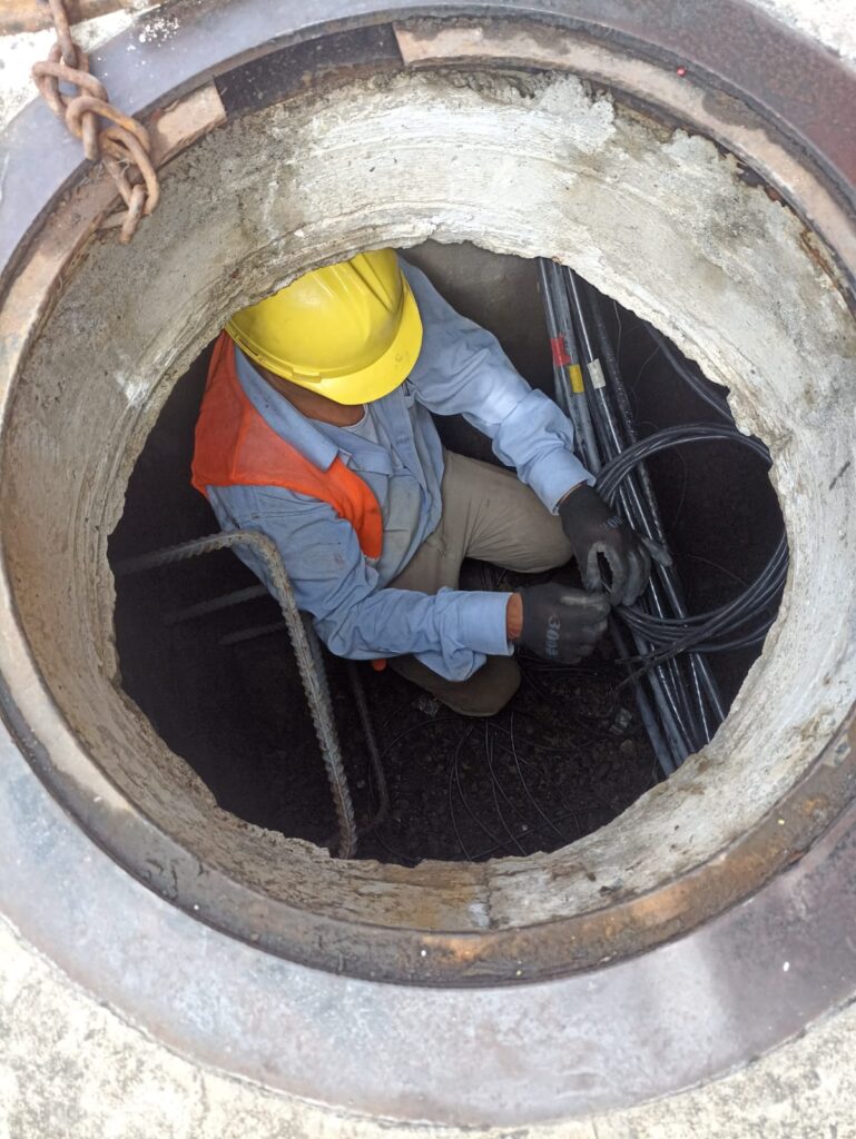 Operario con casco y guantes coloca estoperoles metálicos y cables bajo nivel de calle, para señalización vial en Pereira.