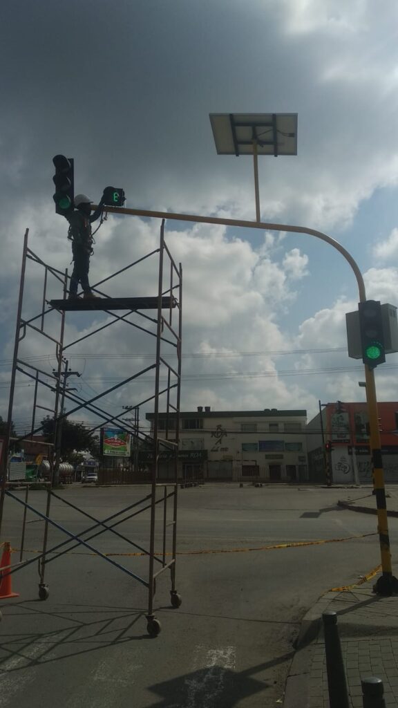 Técnico en escalera ajusta unidad de control y panel solar en poste de semáforo en Madrid.