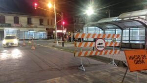Equipo de Smart Planning con conos y cinta amarilla trabajando de noche en semáforo tras poste de parada de buses.