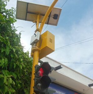 Caja de control semafórico abierto con panel de baterías y componentes internos en poste de semáforo solar.